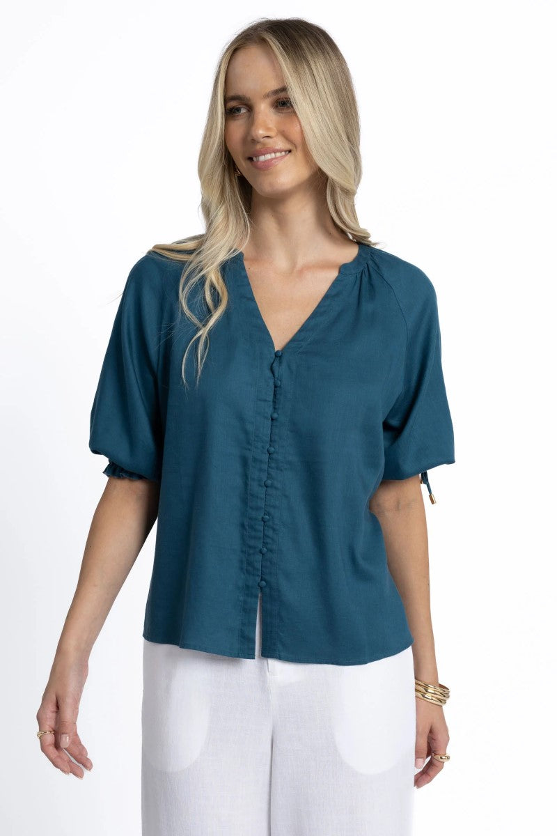 Woman wearing a teal blouse with white pants on a white background