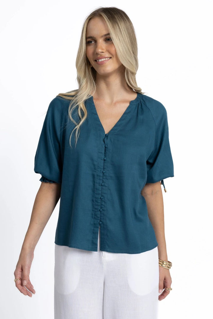 Woman wearing a teal blouse with white pants on a white background