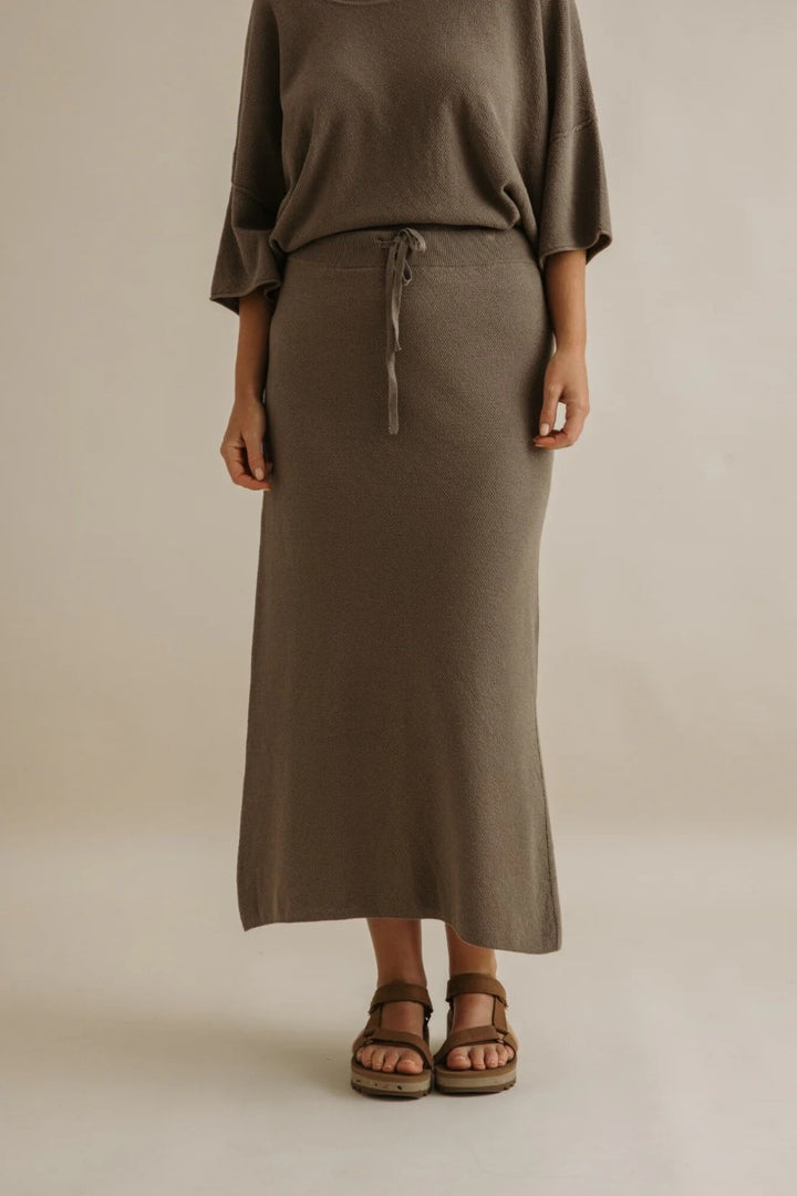 Person wearing a brown long skirt and top against a beige background