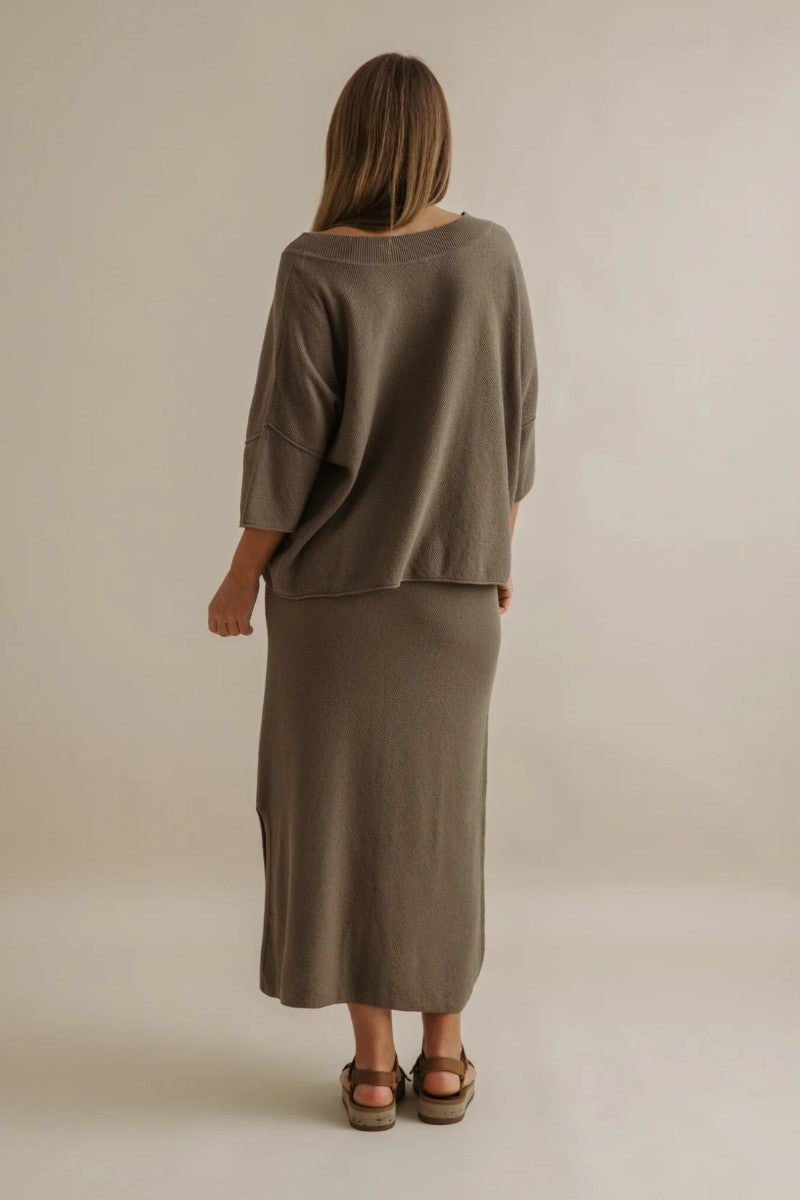 Person wearing a brown outfit standing against a plain background