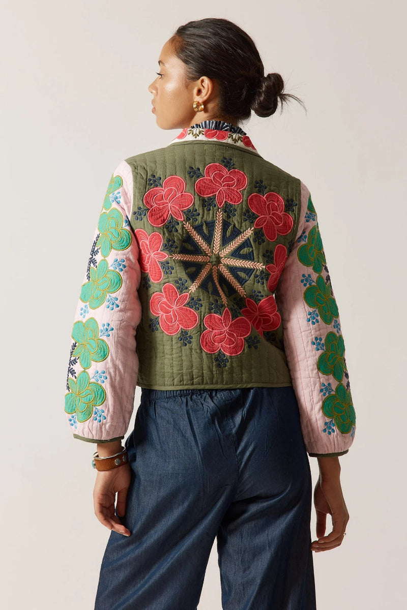 Person wearing a colorful embroidered jacket with floral patterns on a plain background