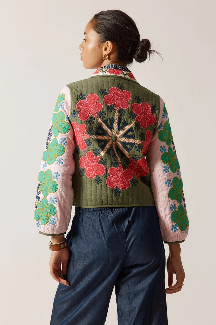 Person wearing a colorful embroidered jacket with floral patterns on a plain background