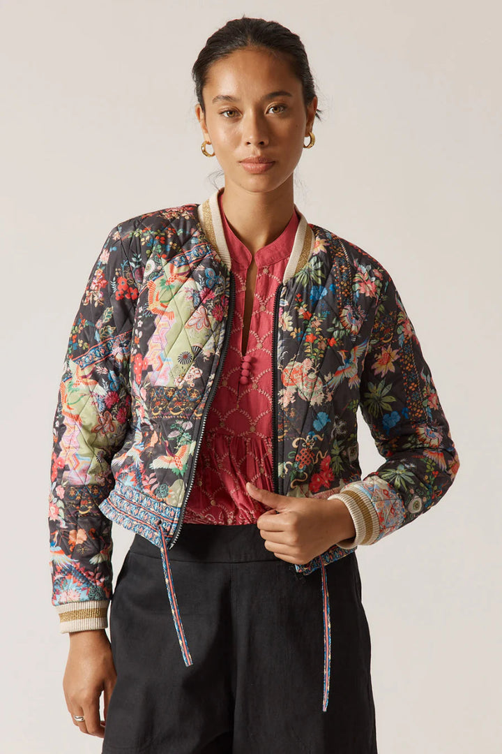 Person wearing a floral bomber jacket over a red top with a plain background