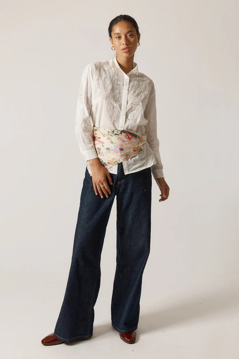 Person wearing a white shirt, floral skirt, and dark pants on a plain background