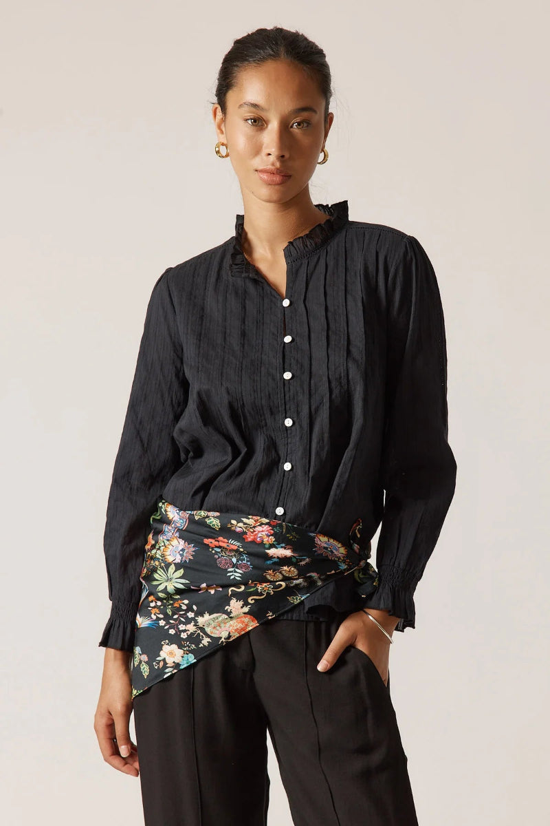 Woman wearing a black button-up shirt with a floral skirt against a plain background