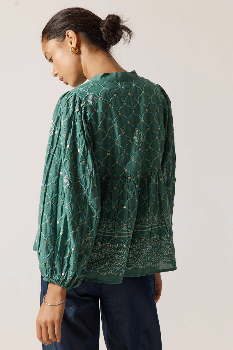 Woman wearing a green patterned blouse against a plain background