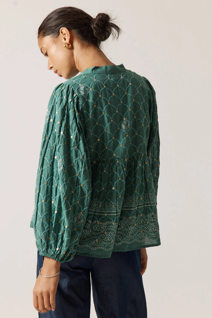 Woman wearing a green patterned blouse against a plain background