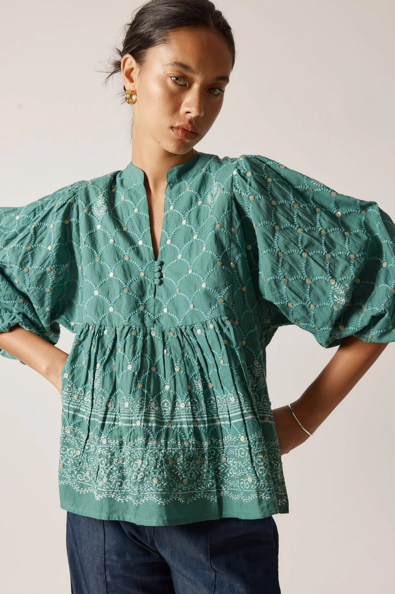 Woman wearing a green blouse with puff sleeves against a neutral background