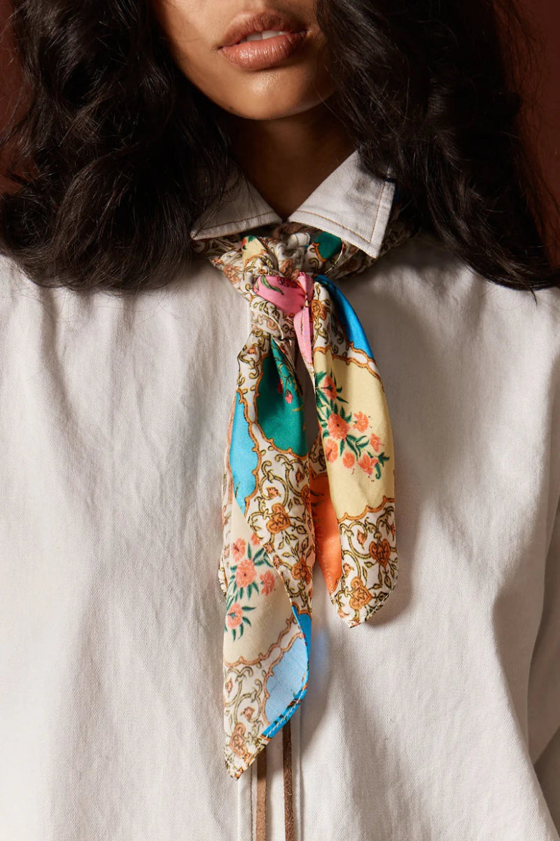 Woman wearing a floral scarf around her neck against a neutral background