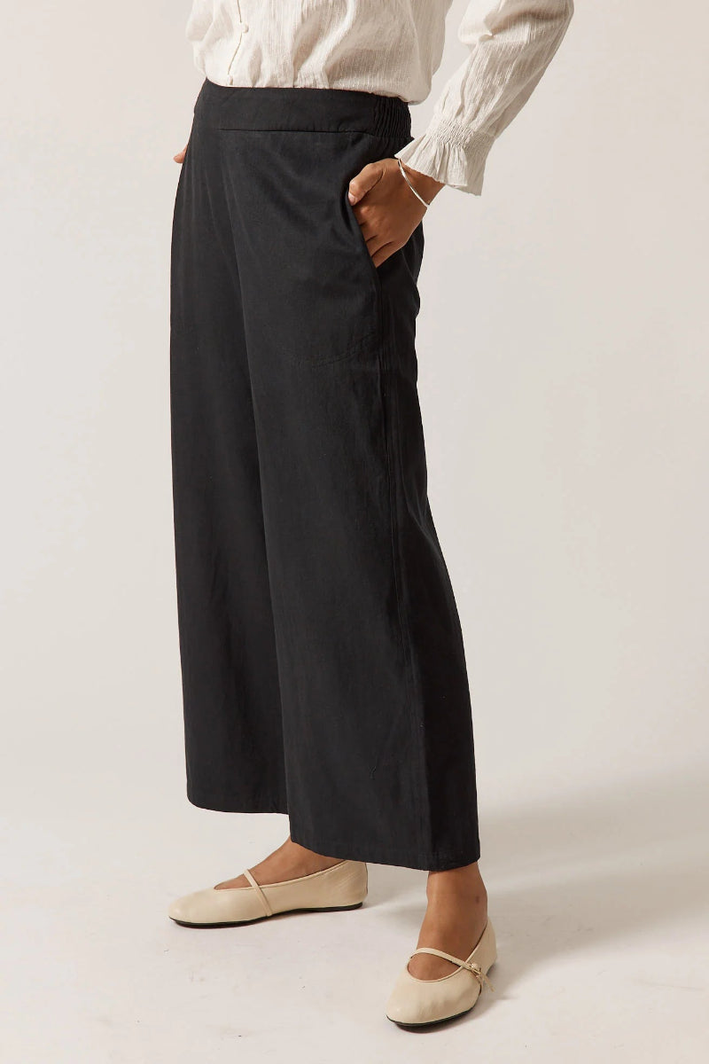 Person wearing black wide-leg pants and a white shirt on a plain background