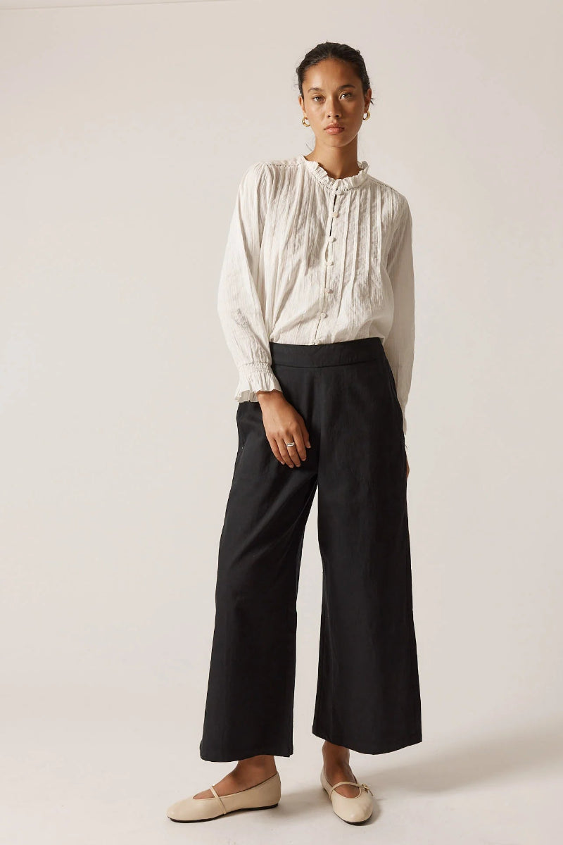 Person wearing a white blouse and black pants on a plain background