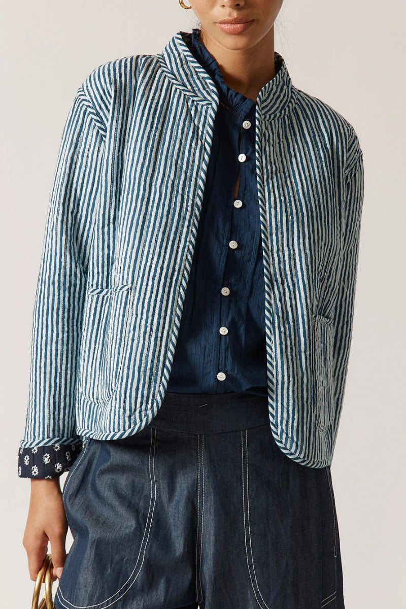 Person wearing a blue and white striped jacket over a dark shirt with a plain background