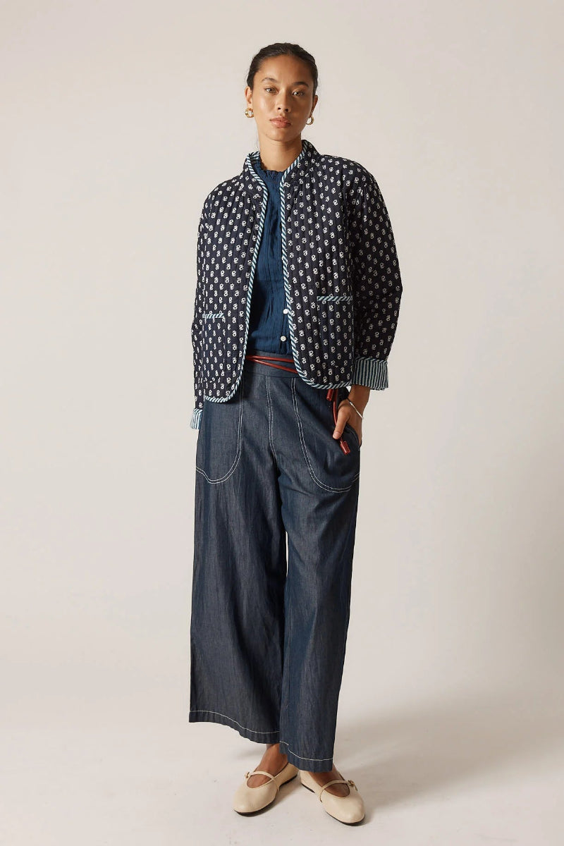 Person wearing a polka dot jacket over a blue sweater and wide-leg jeans on a plain background