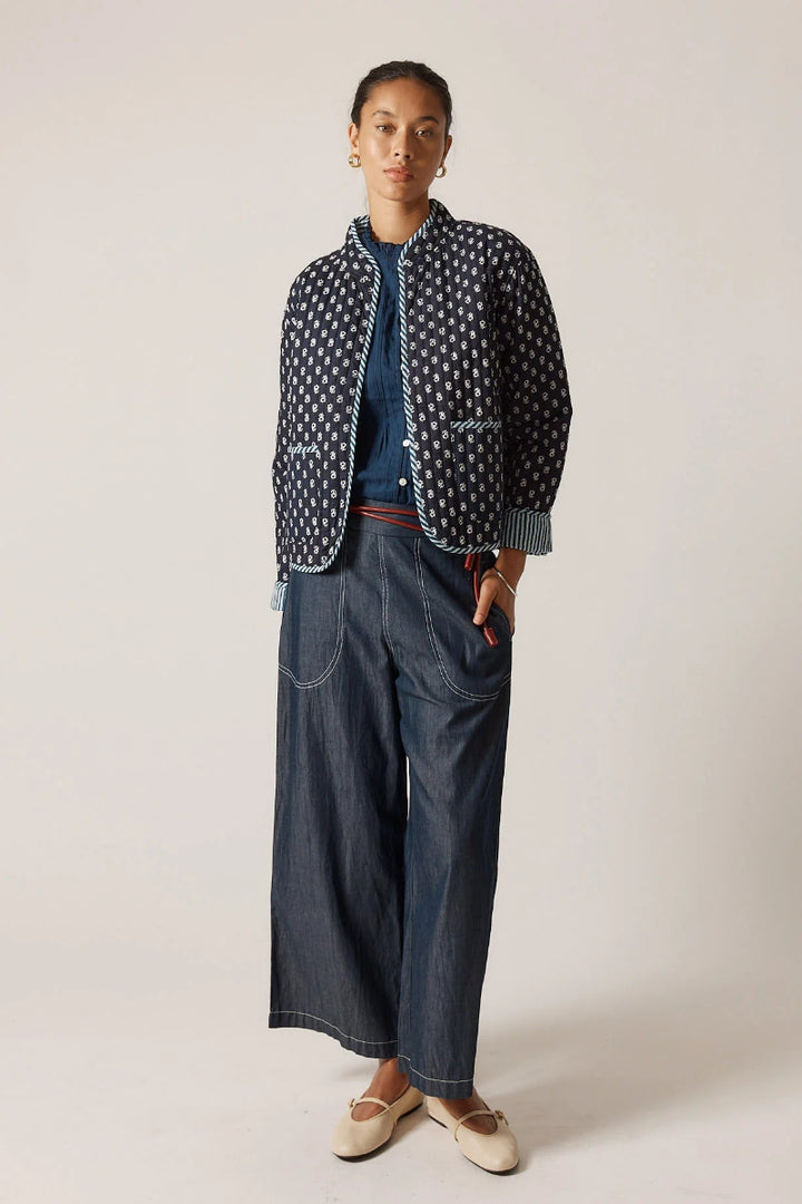 Person wearing a polka dot jacket over a blue sweater and wide-leg jeans on a plain background