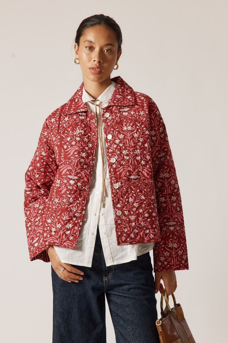 Person wearing a red floral jacket over a white shirt with a plain background