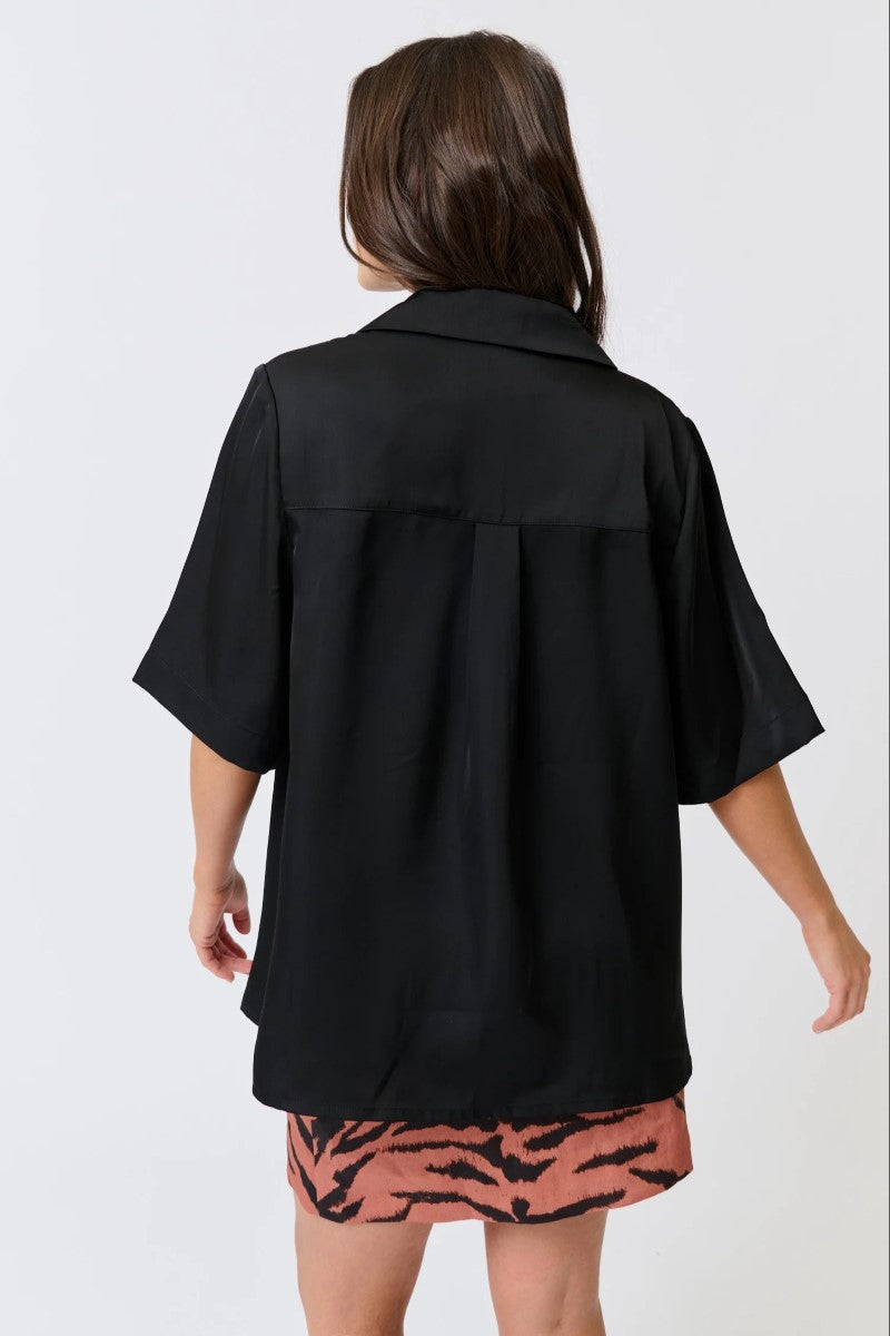 Person wearing a black oversized shirt over a patterned skirt on a white background