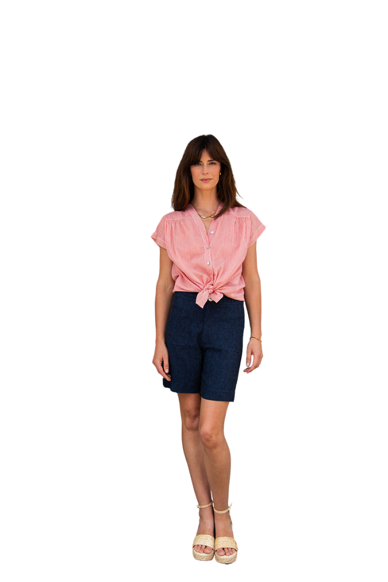 A woman modeling a pink short-sleeve tie-front blouse and dark denim shorts against a plain white background.