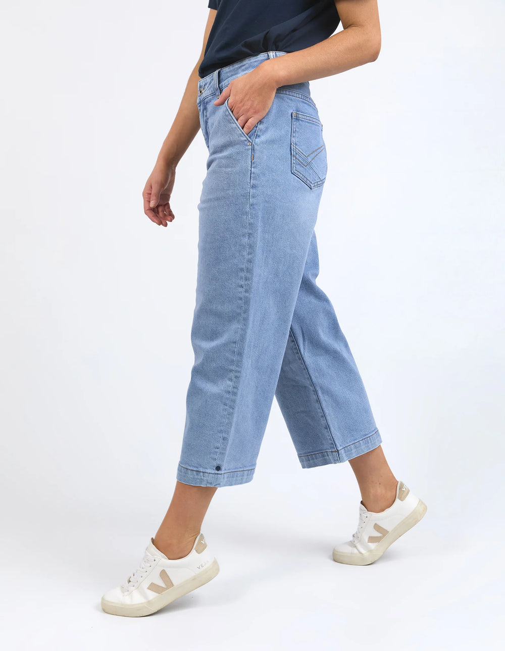 Person wearing light blue jeans and white sneakers on a white background