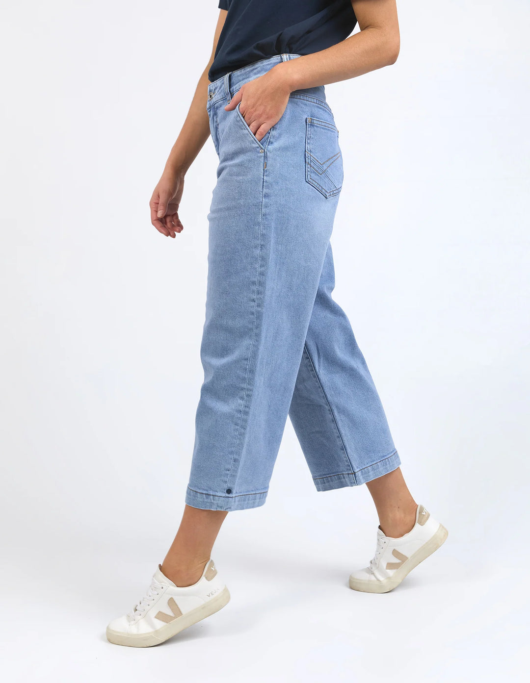Person wearing light blue jeans and white sneakers on a white background