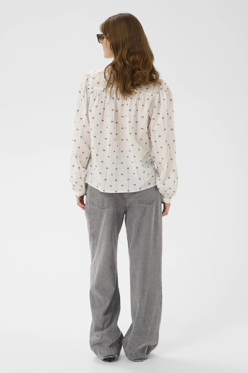 Woman wearing a patterned blouse and gray pants on a white background