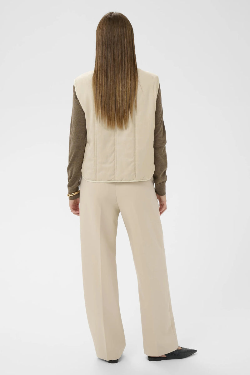 Person wearing a beige vest and pants set on a white background