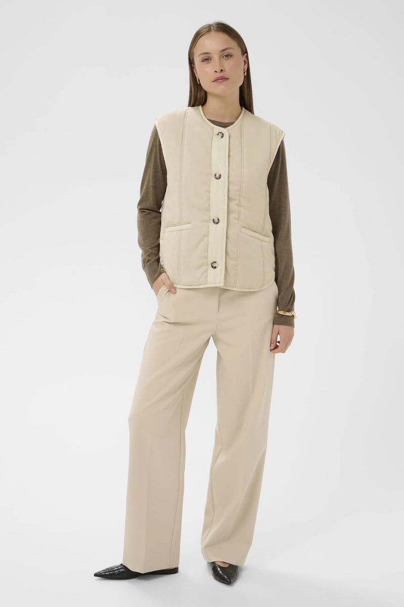 Woman wearing a beige quilted vest over a brown shirt on a white background