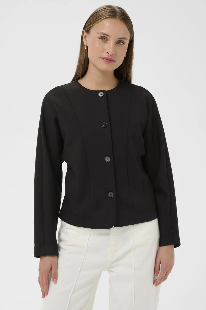 Woman wearing a black jacket and white pants on a light gray background