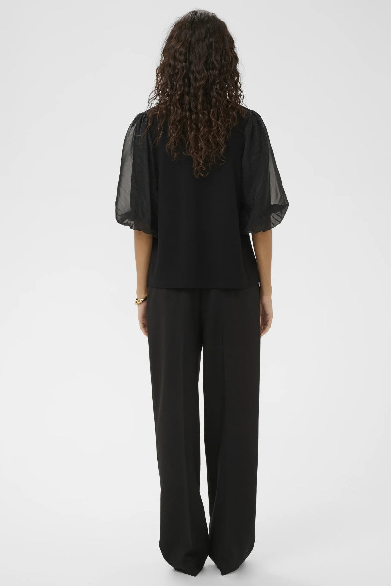 Person wearing a black outfit with sheer sleeves on a white background