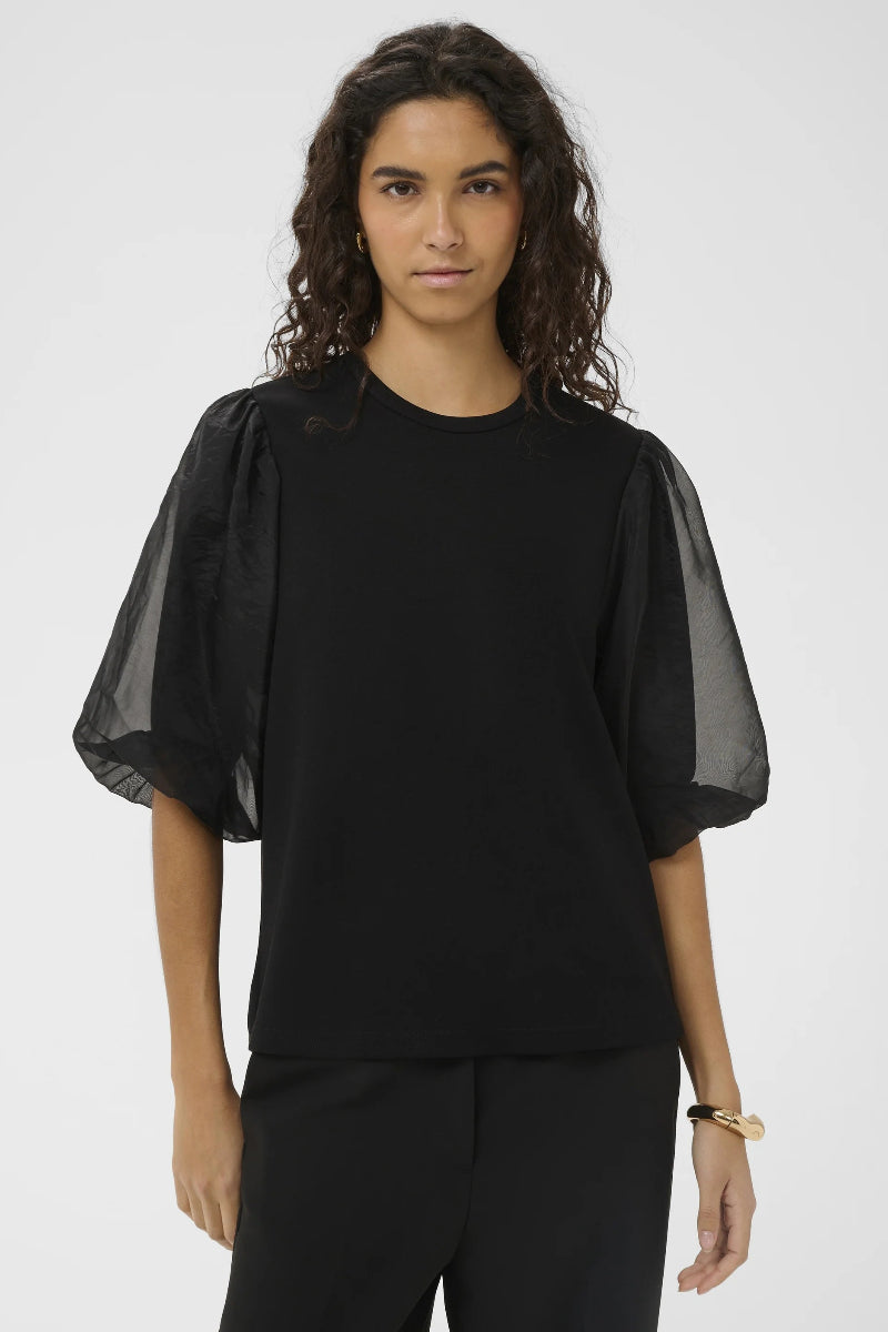 Woman wearing a black outfit with sheer sleeves on a white background