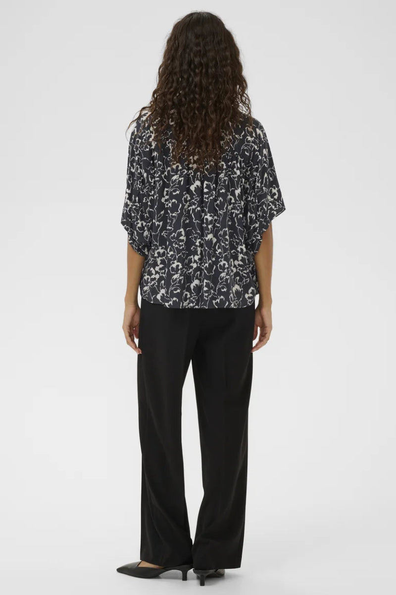 Person wearing a black and white patterned blouse with black pants on a white background