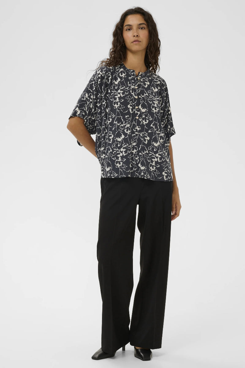 Person wearing a black and white patterned shirt with black pants on a white background