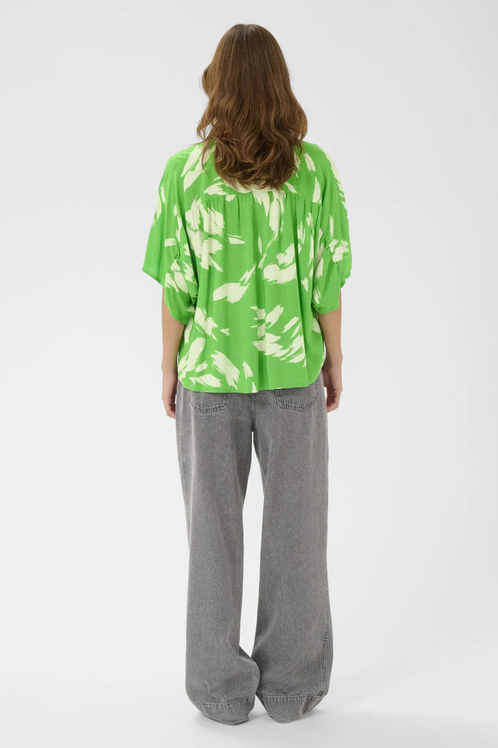 Person wearing a green floral blouse and gray pants on a white background
