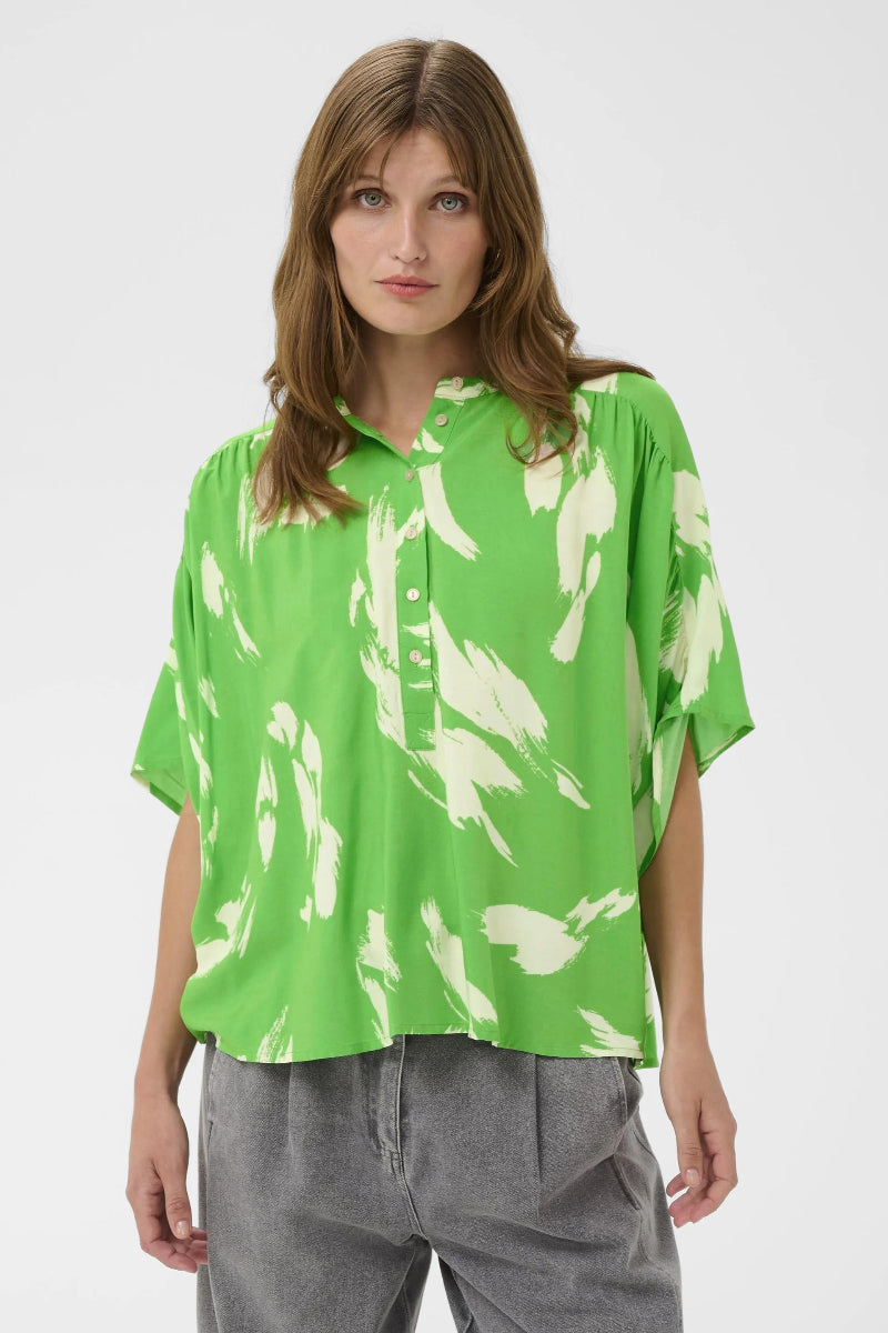 Woman wearing a green blouse with white floral patterns on a plain background