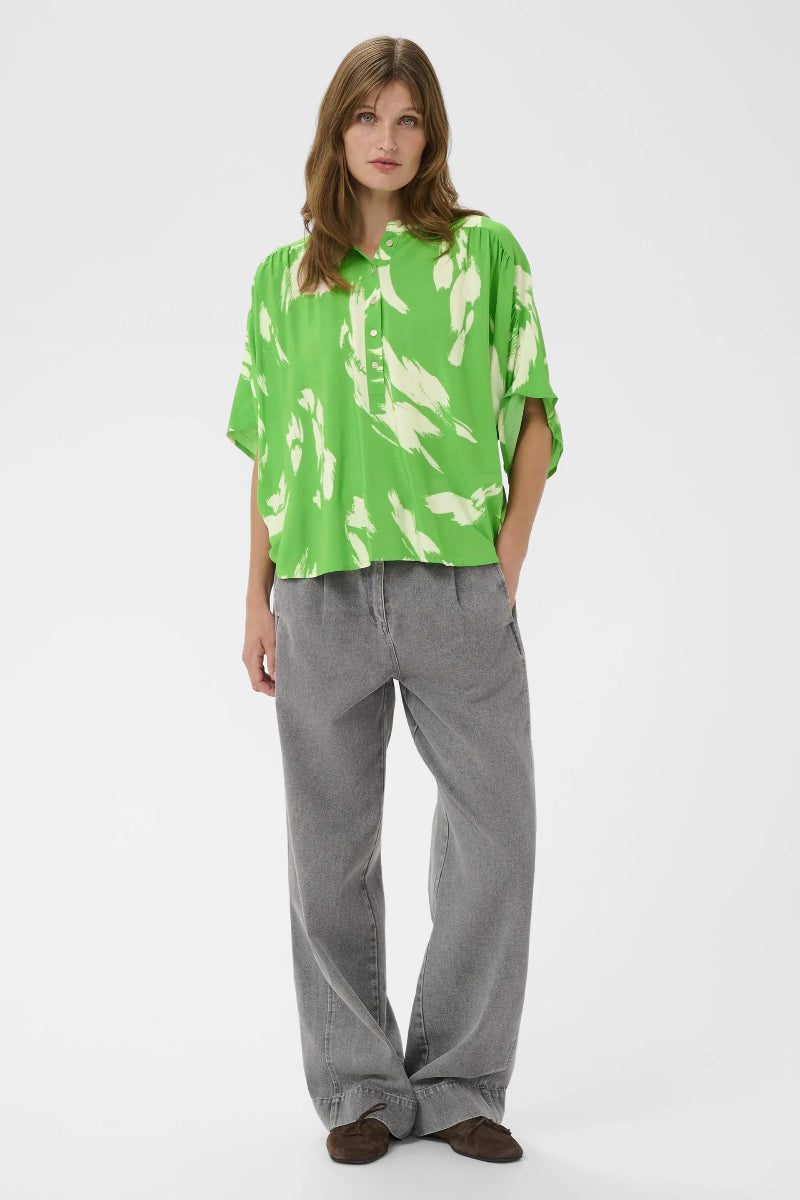 Person wearing a green and white patterned shirt with gray pants on a white background