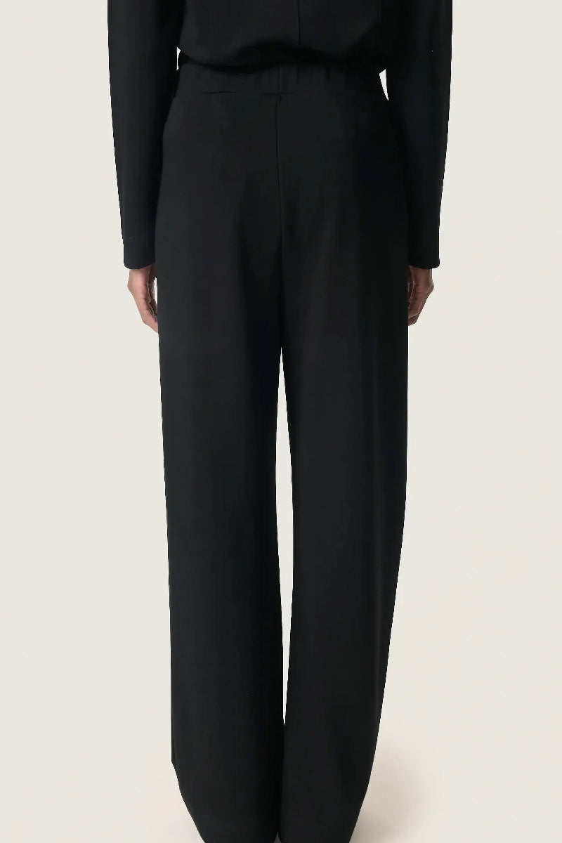 Black suit pants worn by a person on a light beige background
