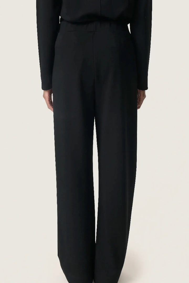 Black suit pants worn by a person on a light beige background