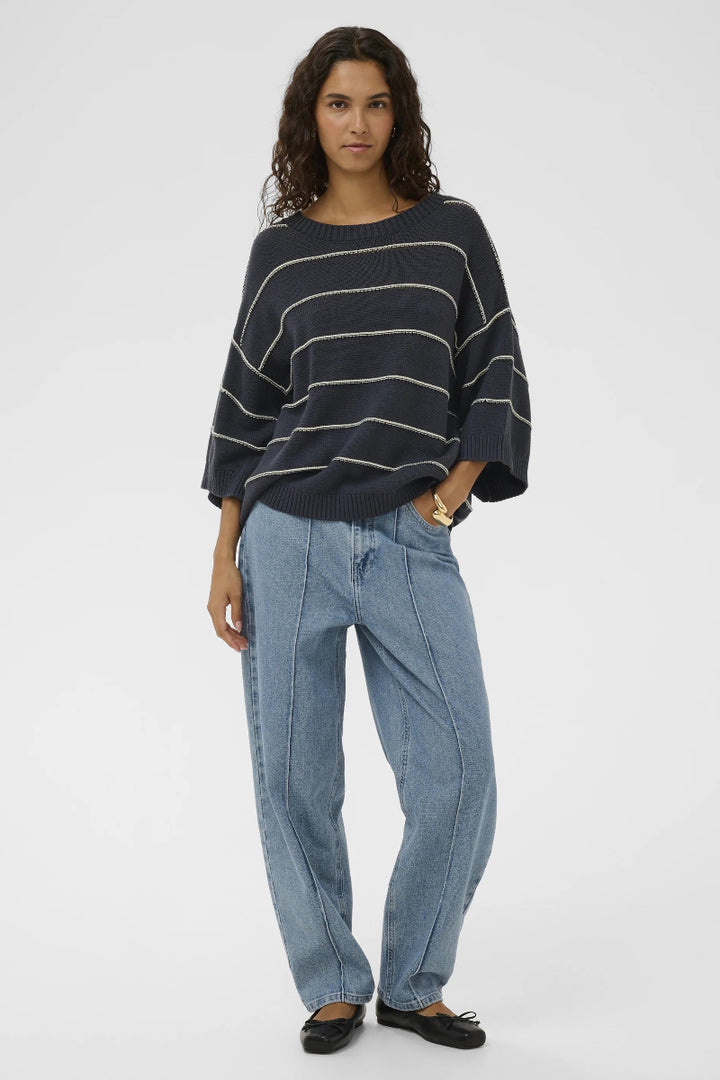 Woman wearing a dark blue striped sweater and light blue jeans on a white background