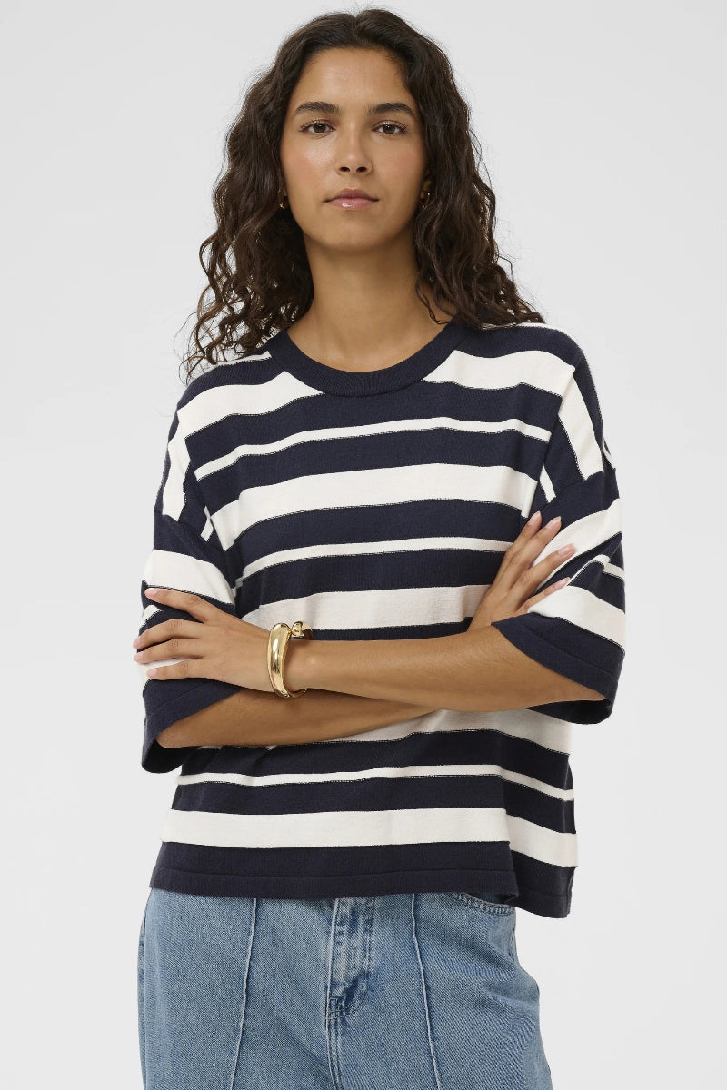 Woman wearing a navy and white striped sweater with blue jeans on a plain background