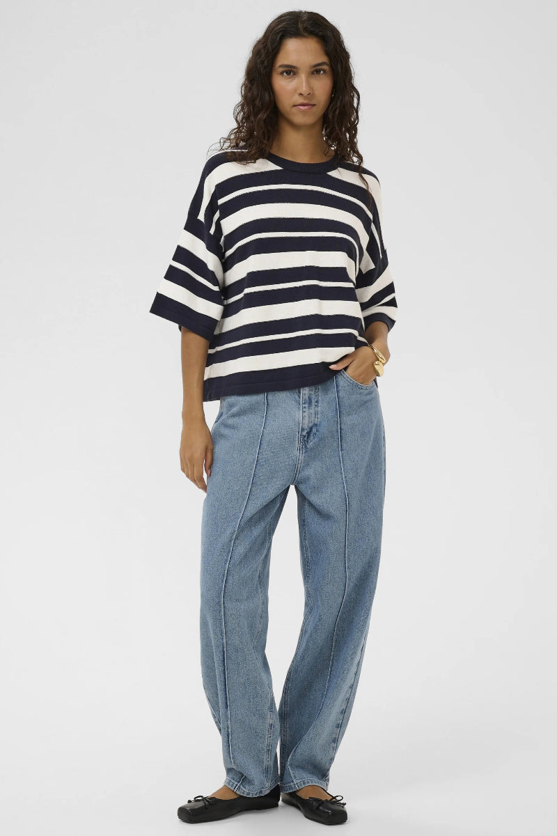 Person wearing a black and white striped sweater and blue jeans on a white background