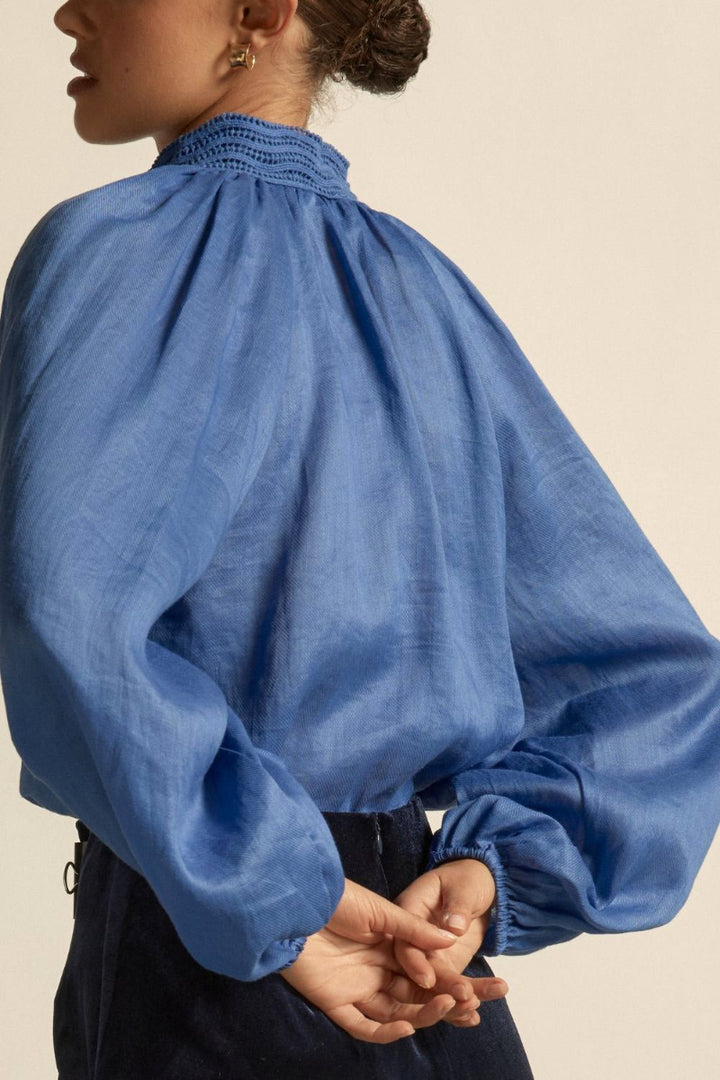 Woman wearing blue button blouse long sleeve, soft collar and black pants back.