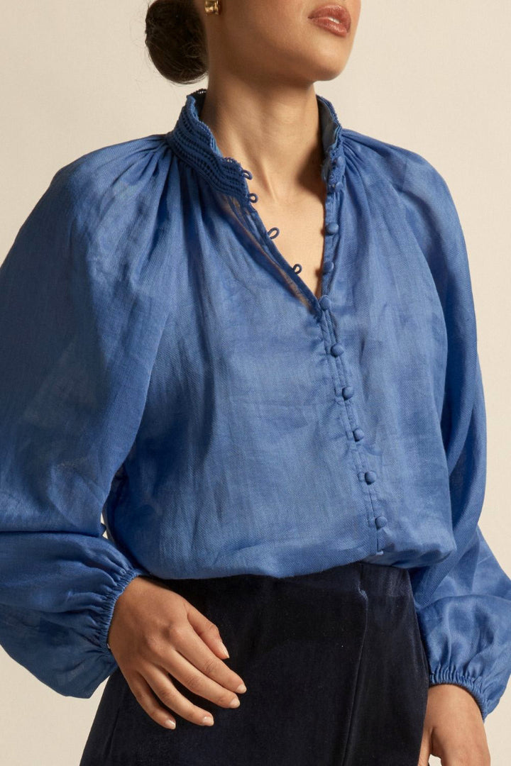 Woman wearing blue button blouse long sleeve, soft collar and a row pf button down the front.