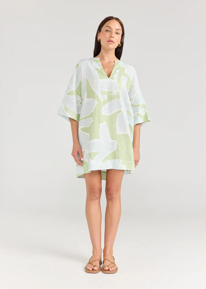 Woman wearing a light green and white patterned dress on a plain background
