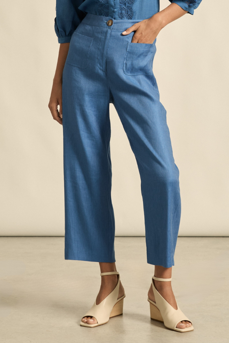 This front close-up view of the Syllabus Pant in Shoreline captures the elegant tailoring, curved patch pockets, and classic waistband with zip and tortoise shell button detail.
