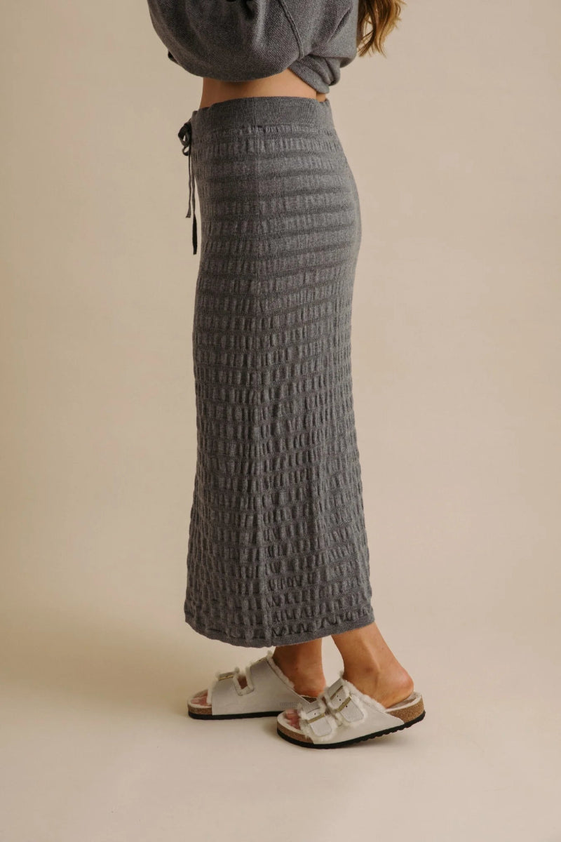 Person wearing a textured gray skirt on a beige background