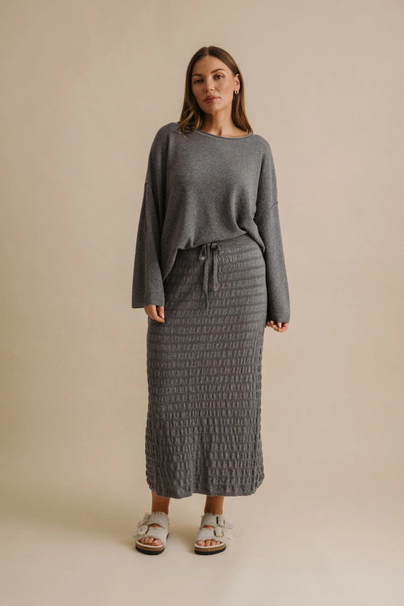 Woman wearing a gray sweater and textured skirt on a beige background