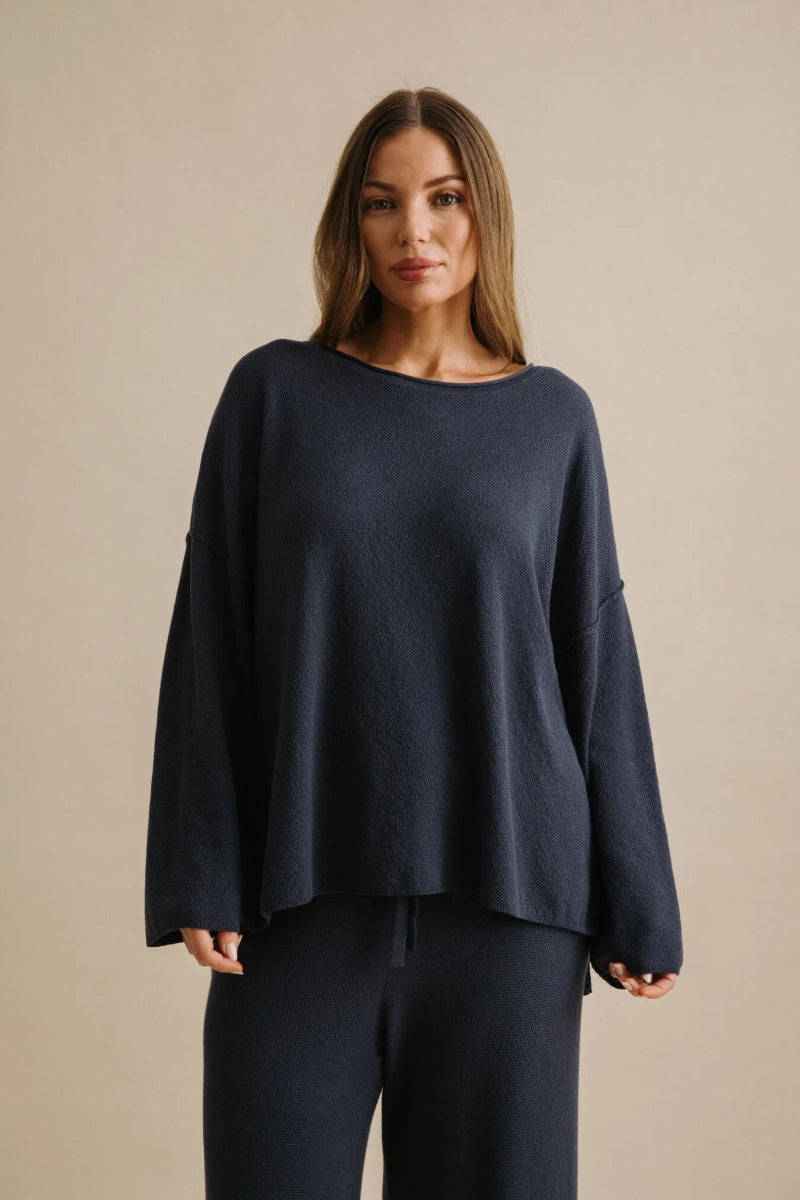 Woman wearing a navy blue sweater and pants against a beige background