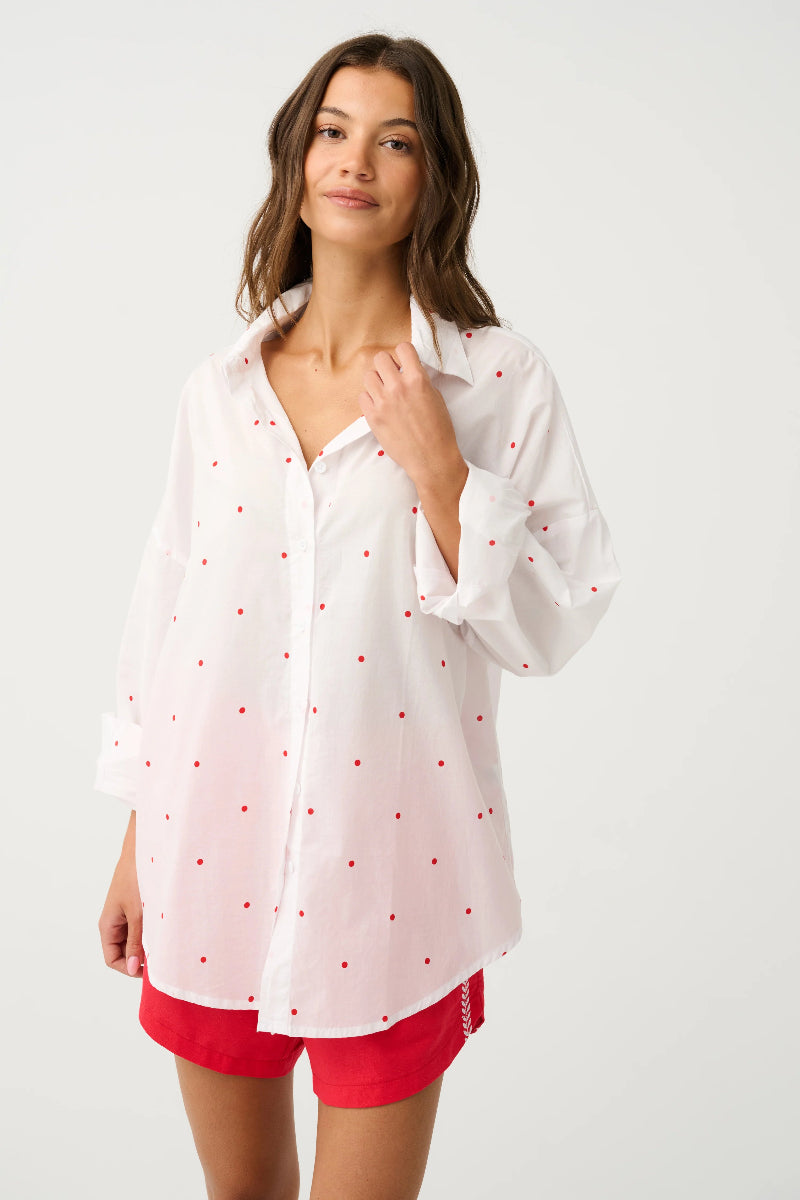 Woman wearing a white shirt with red polka dots and red shorts on a white background