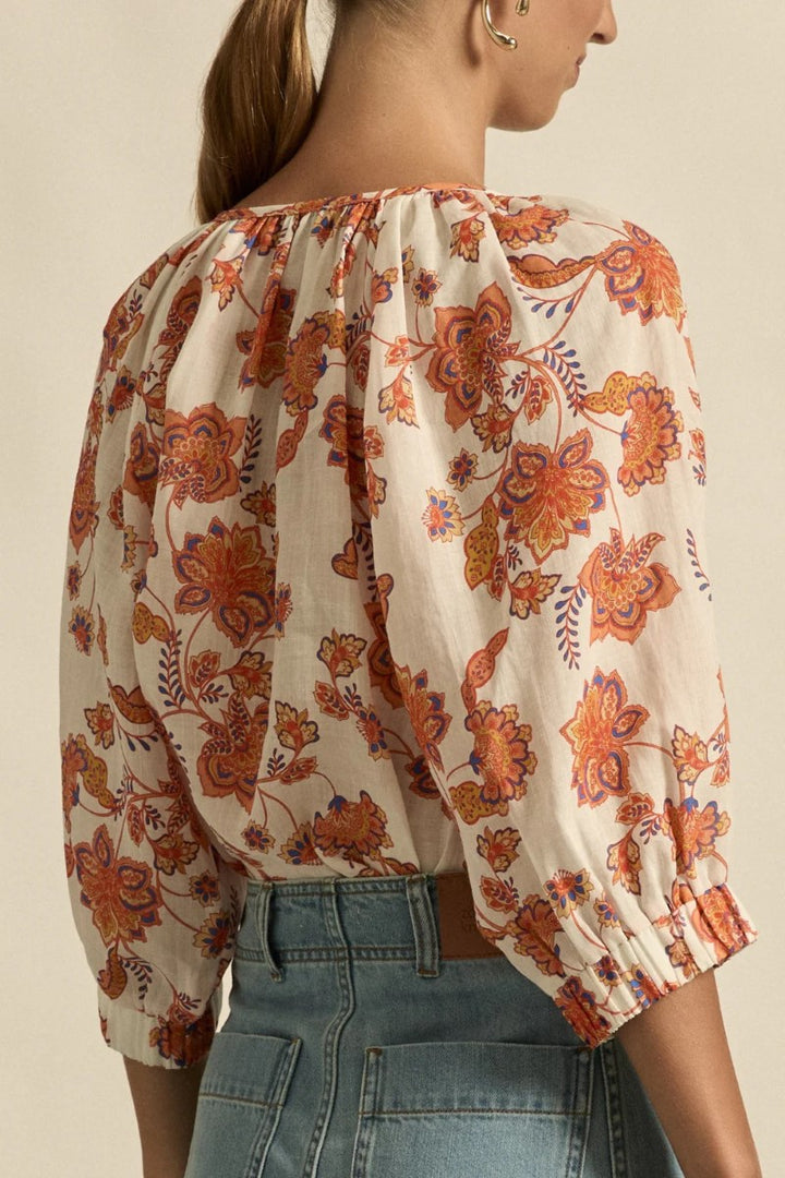 Woman wearing a floral blouse with orange and brown patterns on a beige background
