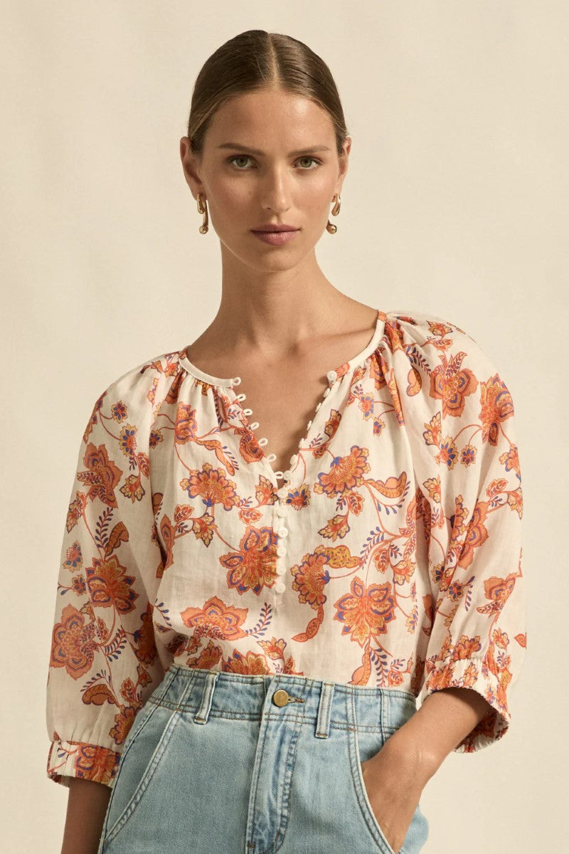 Woman wearing a floral blouse with orange and blue accents on a beige background