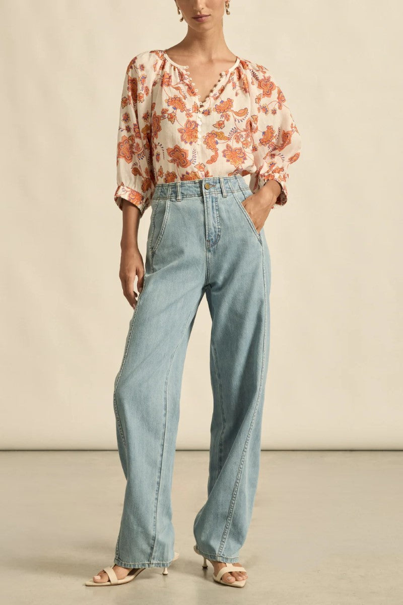 Woman wearing a floral blouse and light blue jeans against a neutral background